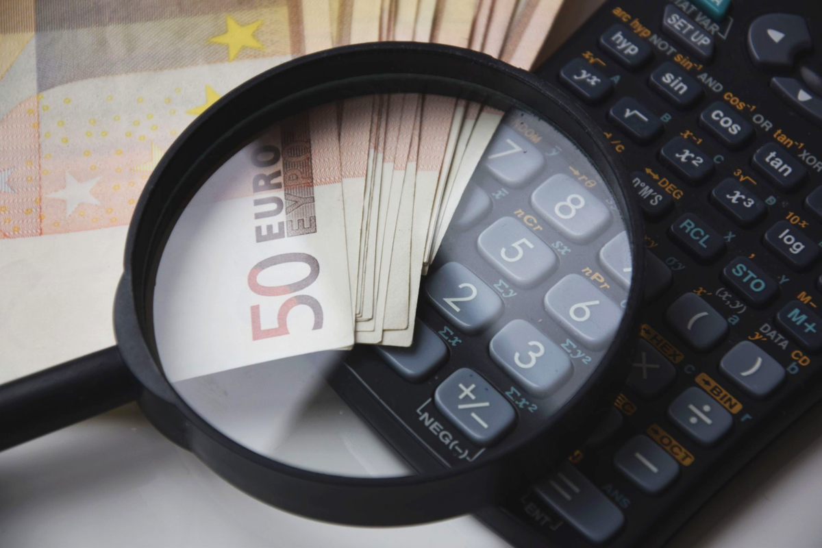 Billets en euros sous une loupe avec une calculatrice, symbolisant les finances et l'analyse.