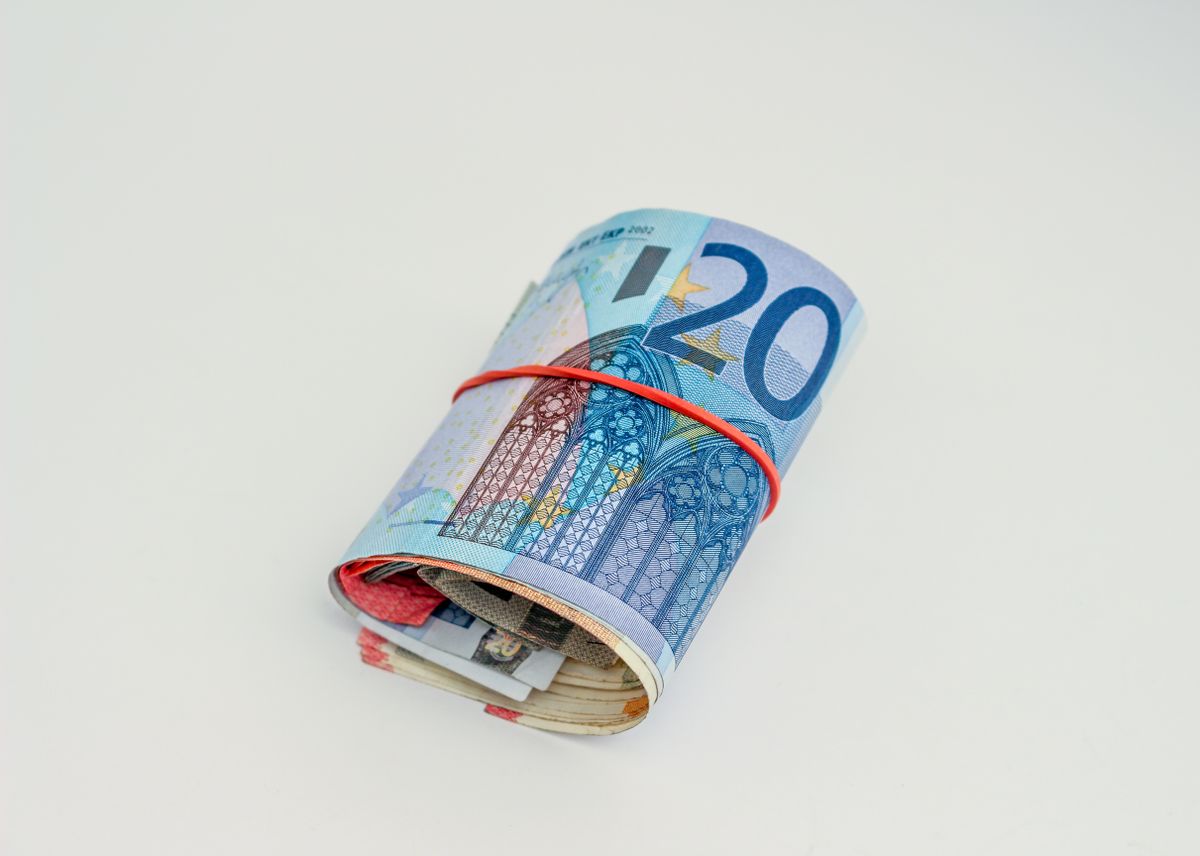 Gros plan de billets en euros roulés maintenus par un élastique rouge sur fond blanc.