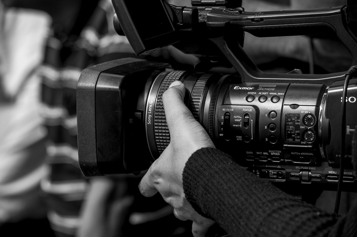 Image en noir et blanc d'une personne utilisant une caméra vidéo professionnelle, présentant les commandes détaillées de la caméra.