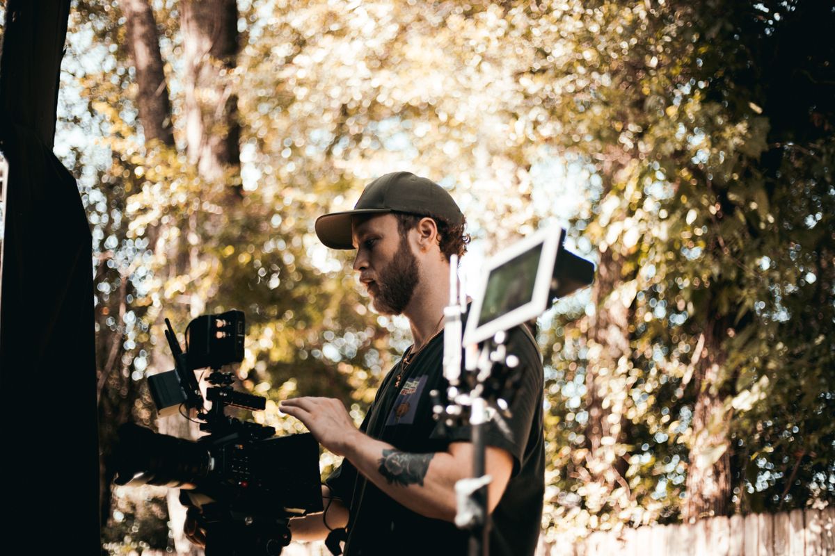 Cinematographer in action adjusting camera setup outdoors with foliage background.