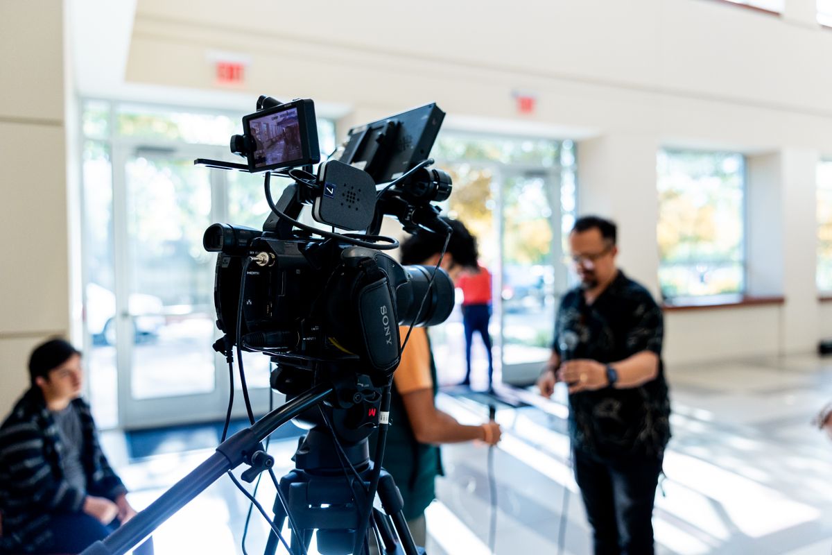 Close-up of a professional video camera on a tripod with people blurred in background