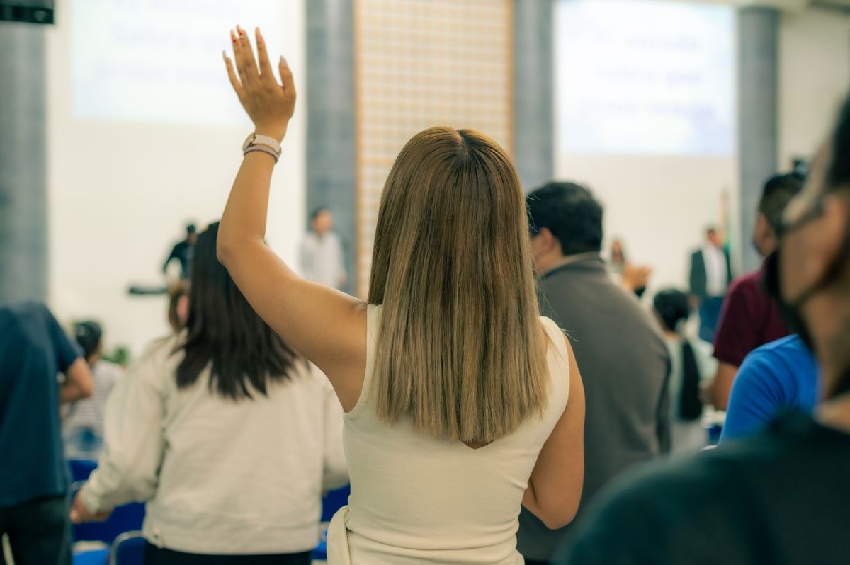 Back view of a woman raising hand during an indoor event, showcasing engagement.