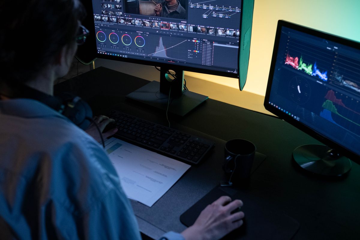 A video editor using dual monitors for editing footage in a dimly lit studio.