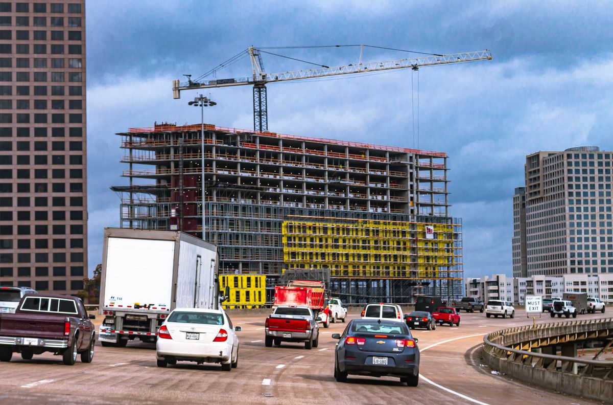 Dynamic cityscape of a busy road with moving traffic and a construction site against a cloudy sky.