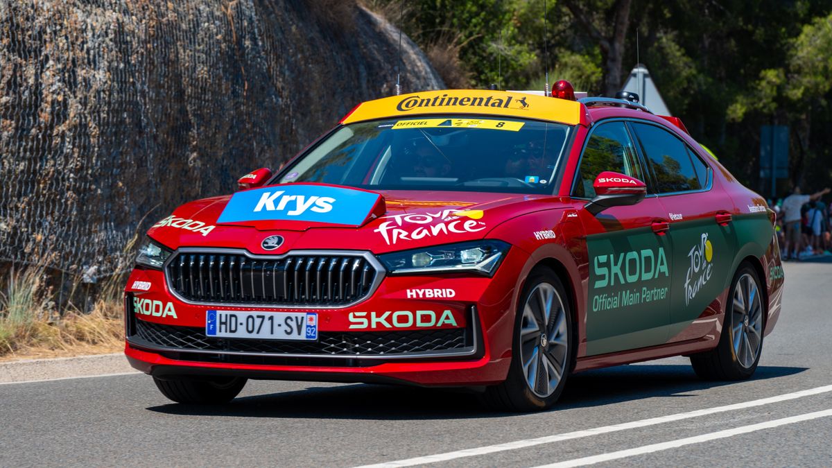 Voiture d'assistance ŠKODA rouge sur le Tour de France, arborant des autocollants de la marque sur un parcours panoramique.