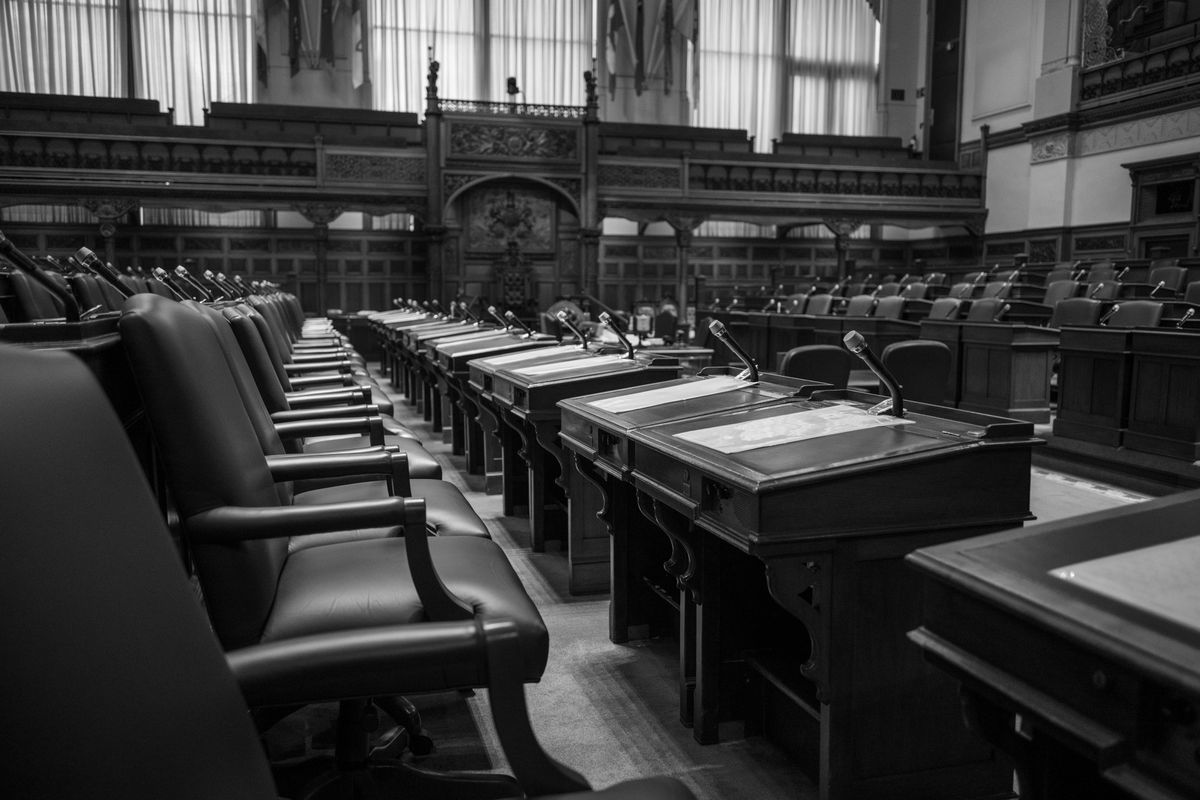 Photographie en noir et blanc d'une salle d'assemblée législative traditionnelle, avec des sièges et des bureaux vides.